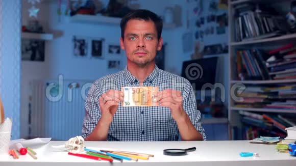 一个男人坐在桌子旁拿出一张50欧元的钞票视频的预览图