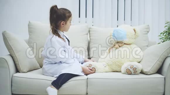 小女孩在玩她的泰迪她是个医生熊是个病人女孩正在用听诊器检查她的泰迪视频的预览图
