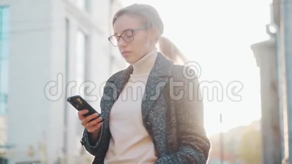 一个手里拿着智能手机的年轻女人的肖像女孩在户外使用手机视频的预览图