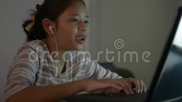 亚洲可爱的女孩学生戴着耳机在网上学习课程时与笔记本电脑老师交谈视频的预览图