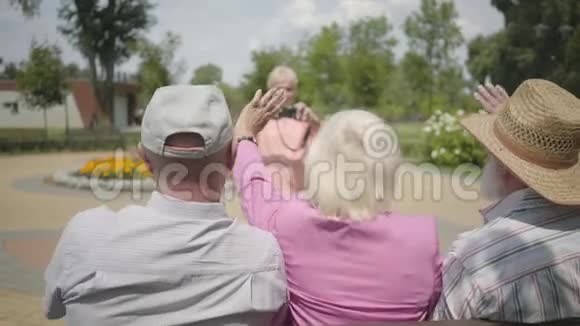 两个年长的男人和一个女人挥手而第四个女人在公园里给他们拍照成熟的人视频的预览图