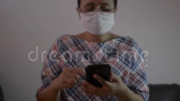 女士戴着防护面罩使用手机智能手机在客厅的社交网络上进行交流视频的预览图