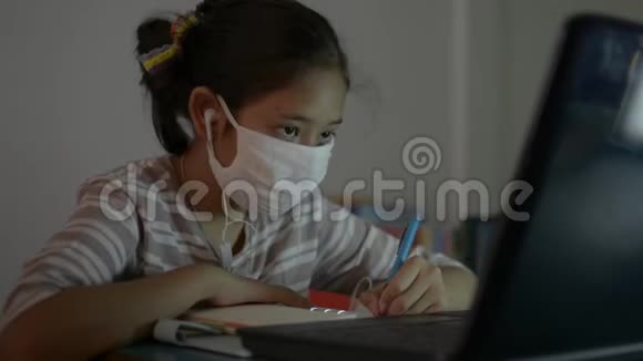 亚洲可爱的女孩戴着耳机在做家庭作业时从笔记本电脑上在线观看课程视频的预览图