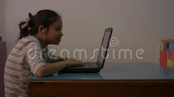 亚洲可爱的女孩学生戴着耳机在网上学习课程时与笔记本电脑老师交谈视频的预览图