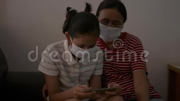 母亲和女儿戴着防护面具坐在家里进行检疫以防止COVID19大流行视频的预览图