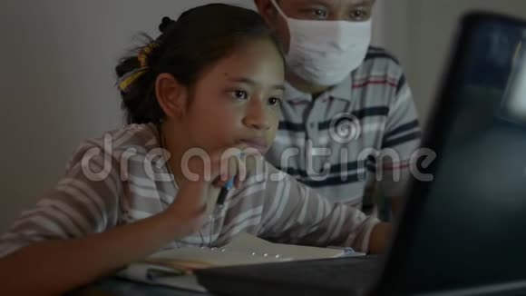 亚洲可爱的女孩和她的父亲在做家庭作业时从笔记本电脑上在线看课视频的预览图
