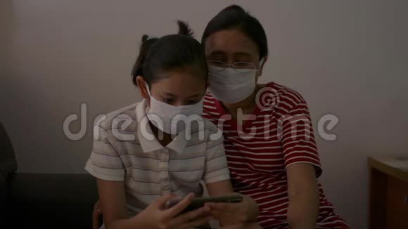 母亲和女儿戴着防护面具坐在家里进行检疫以防止COVID19大流行视频的预览图