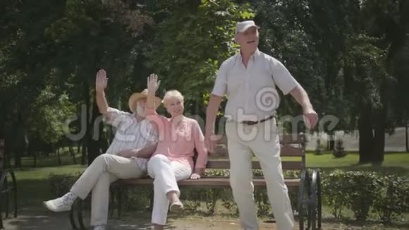 两个年长的男人和一个女人挥舞着手而他们的朋友女人在公园里骑滑板车成熟的人休息视频的预览图