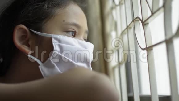 亚洲可爱的女孩戴着防护面具绝望地看着窗外的COVID19疫情视频的预览图