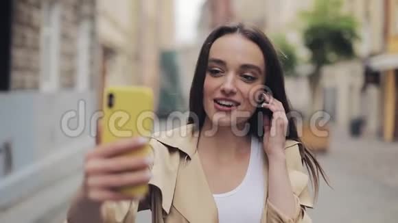 美丽的微笑的年轻女士戴着耳机摸着他们打着视频电话拿着电话垂直交谈视频的预览图