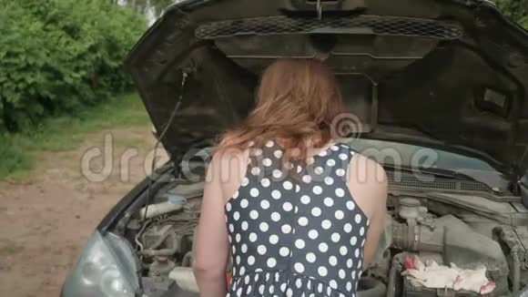 后面的女孩穿着有斑点的衣服靠近汽车带着打开的引擎盖女孩笑着转过身来擦了擦额头视频的预览图
