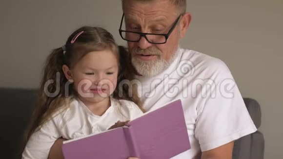 祖父戴眼镜的肖像画和可爱的小孙女坐在一起看书视频的预览图