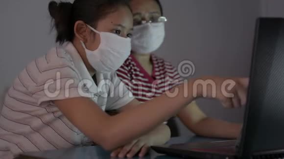 亚洲可爱的女孩她的母亲戴着保护面具在做家庭作业时从笔记本电脑在线观看课程视频的预览图