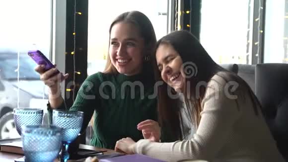 年轻开朗的女孩最好的朋友正坐在咖啡馆里用智能手机笑着视频的预览图