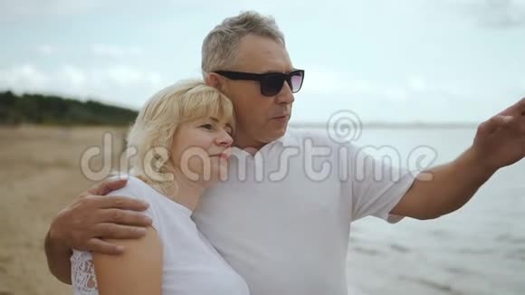 年老的女人和男人拥抱着看着远处的海滩视频的预览图