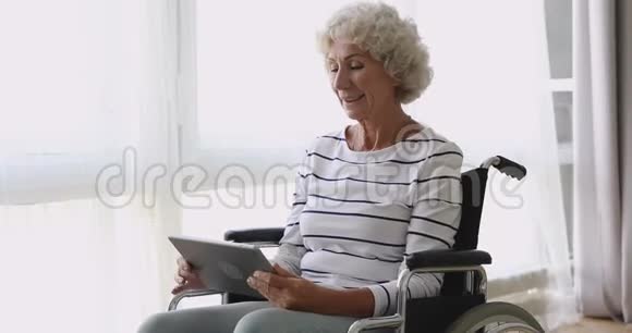 快乐的老年妇女坐在轮椅上使用数字平板电脑视频的预览图