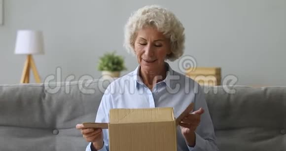 快乐的老年妇女打开客厅的包裹视频的预览图