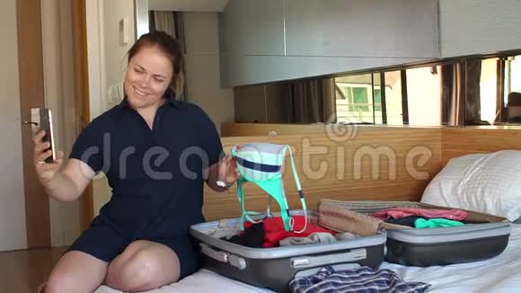 年轻女子用泳衣在卧室里用手提箱做自拍视频的预览图