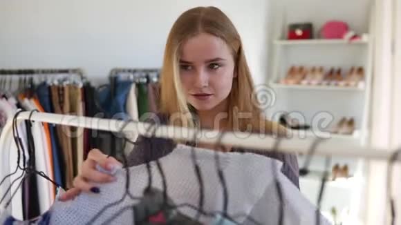 金发女孩正在服装店购物她拿着时髦的布衣架看上去很神气视频的预览图
