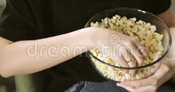 年轻的女人从玻璃透明的碗里吃新鲜的爆米花双手特写视频的预览图