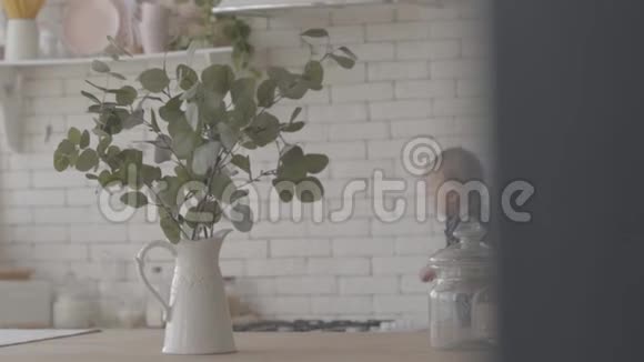 年轻的母亲在厨房里抱着婴儿前景中有绿叶的花瓶快乐的妈妈和可爱的视频的预览图