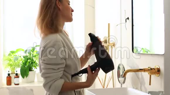 女孩用吹风机在明亮的浴室里烘干头发3年轻女孩明天早上上班视频的预览图