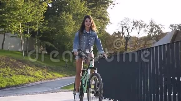 可爱的微笑的热辣女孩穿着牛仔裤的衣服骑自行车靠近金属栅栏视频的预览图