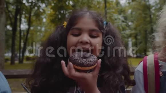 有趣的非裔美国女学生在公园吃巧克力甜甜圈带着快乐的情绪视频的预览图