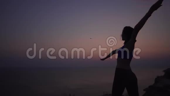 一个女孩练习瑜伽直到太阳在山上的海洋边黎明阿萨纳两臂向两侧稳定射击视频的预览图