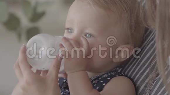 特写肖像美丽微笑的年轻女子从厨房的小婴儿瓶里喂她的女婴概念视频的预览图
