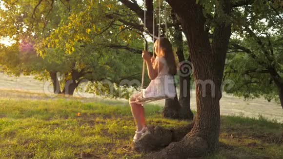 快乐的童年概念孩子在日落公园的橡树枝上飞绳秋千女孩笑高兴年轻女孩视频的预览图