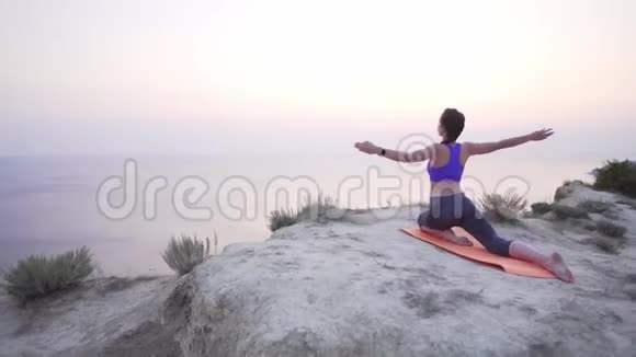 白种人年轻女孩在日出时在海边的山上练习瑜伽穿紫色上衣的女运动员穿着紧身衣视频的预览图