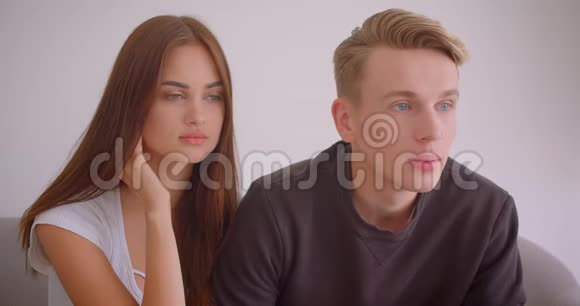 一对年轻的白种人夫妇兴奋地坐在公寓里的沙发上看电视的特写照片视频的预览图
