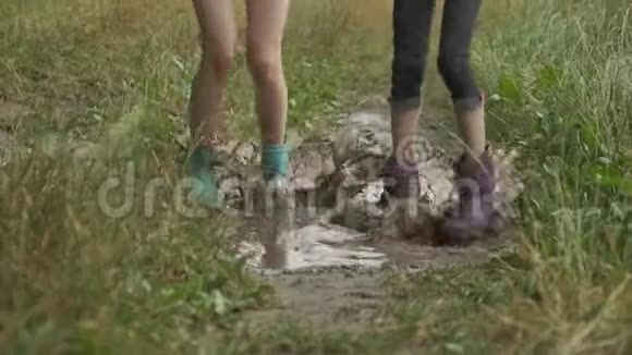 两个穿着靴子的女孩在乡间小路上的雨坑里跳着的腿视频的预览图