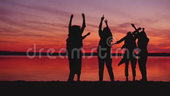 快乐的朋友在黑暗中的海滩上跳舞背景是日落视频的预览图