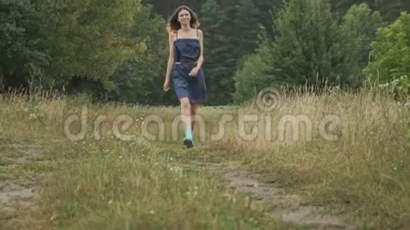 走着年轻的少女穿着裙子和靴子在乡间的道路上自然背景乡村风格视频的预览图