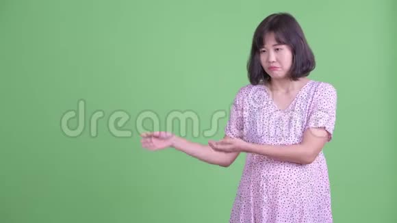 穿着衣服的亚洲孕妇展示一些东西并竖起大拇指视频的预览图
