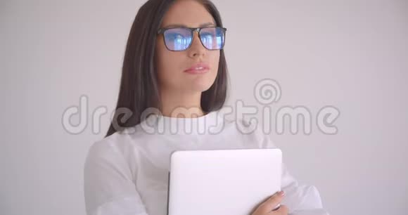 年轻漂亮的白种人女商人戴着眼镜拿着笔记本电脑满怀信心地看着照相机的特写照片视频的预览图