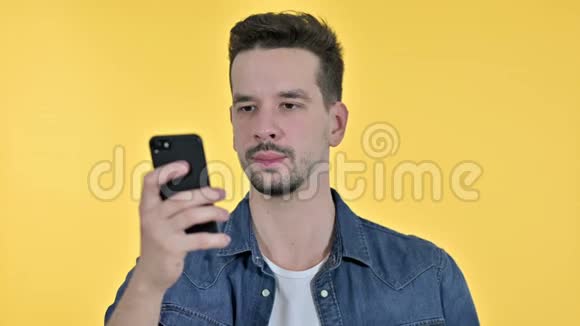 年轻人在智能手机上庆祝成功的肖像黄色背景视频的预览图