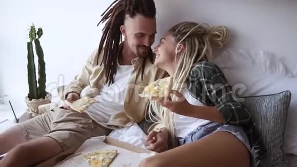 年轻的情侣在卧室里玩得很开心吃送披萨互相喂饭躺在床上度过周末的早晨视频的预览图