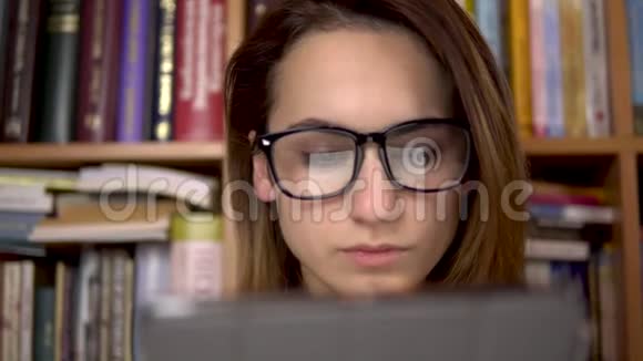一个年轻的女人正在平板电脑里读一本书一个戴眼镜的女人仔细地看着平板电脑在背景中视频的预览图