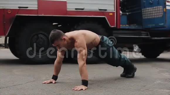 慢动作漂亮的赤膊青年运动员用跳跃练习俯卧撑背景中的大型消防车视频的预览图