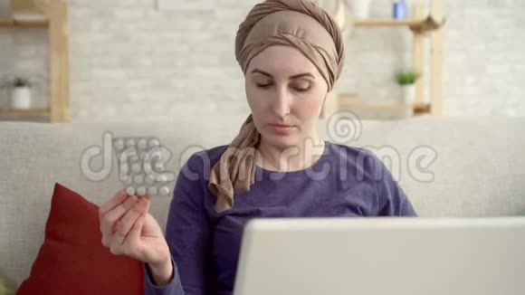 患有癌症的年轻女性在化疗后戴着围巾手里拿着药丸她用笔记本电脑把自己的身体合上视频的预览图