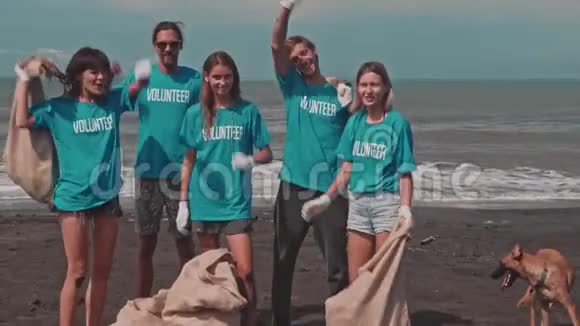 身穿蓝色生态T恤衫的志愿者庆祝海滩垃圾的胜利视频的预览图