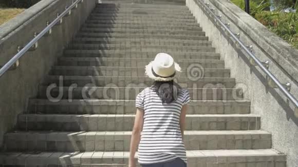 亚洲可爱的女孩穿着休闲装戴着草帽走在楼梯上观景塔跟随慢动作镜头视频的预览图
