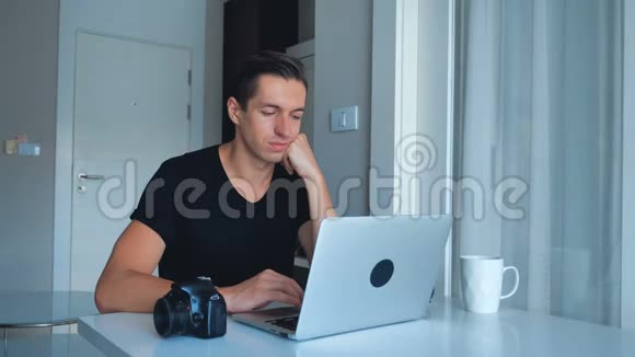 年轻的摄影师使用笔记本电脑处理图像在他的笔记本电脑和喝咖啡在家里外部硬盘摄像头视频的预览图