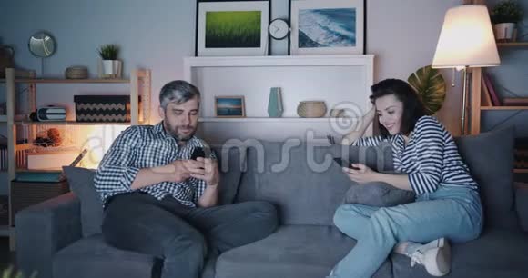 晚上男人和女人在电视前使用智能手机视频的预览图