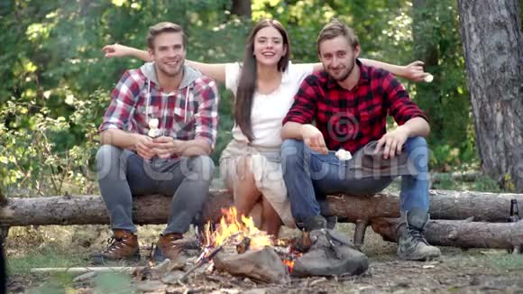 年轻人在篝火旁露营时吃烤棉花糖朋友露营的概念青年群体视频的预览图
