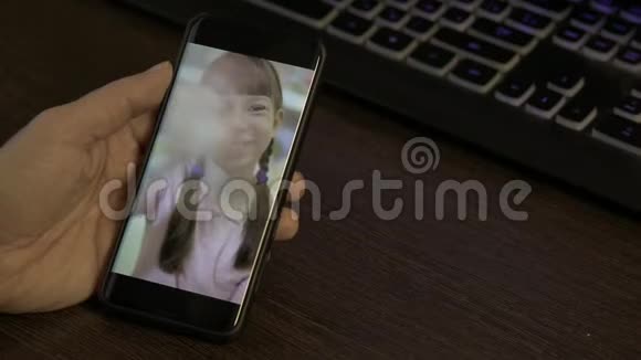 一个男人手里拿着一部智能手机通过视频聊天与女儿交流视频的预览图