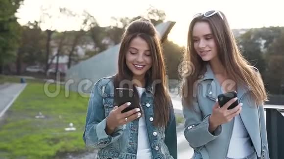 两位年轻迷人的女性朋友的画像她长着长发一边笑着看着一边用智能手机视频的预览图